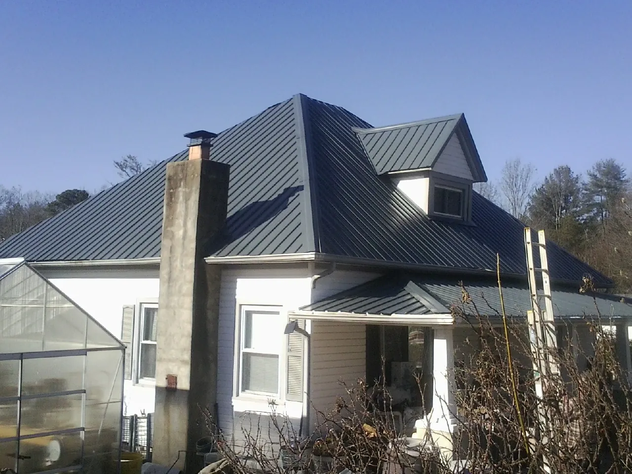 Dark blue standing seam metal roof on a white farmhouse with dormer — Slate & Tile Roof Repair by Roofing Brothers in Woodland Park