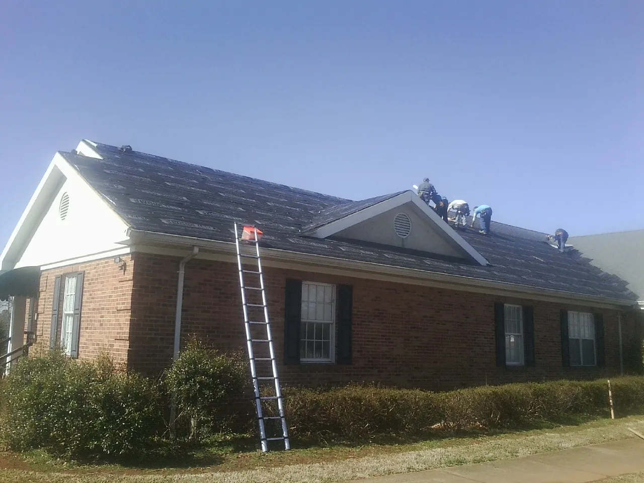 Crew tearing shingles off a brick ranch roof with a ladder set — Metal Roof Repair work by our crew in Woodland Park