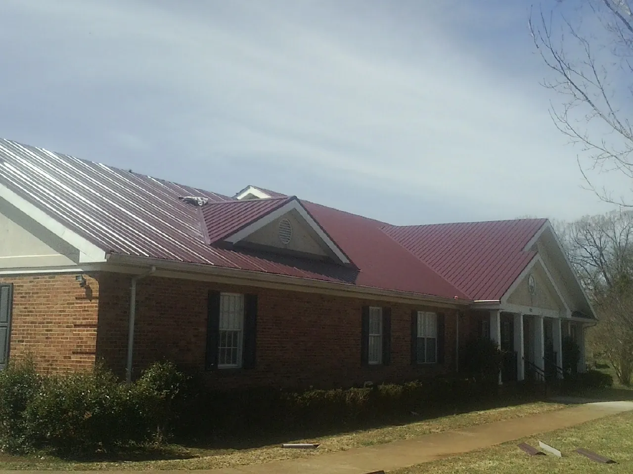 Red metal roof with gabled entries on a long brick building, from a Hail Damage Roof Repair job in Woodland Park
