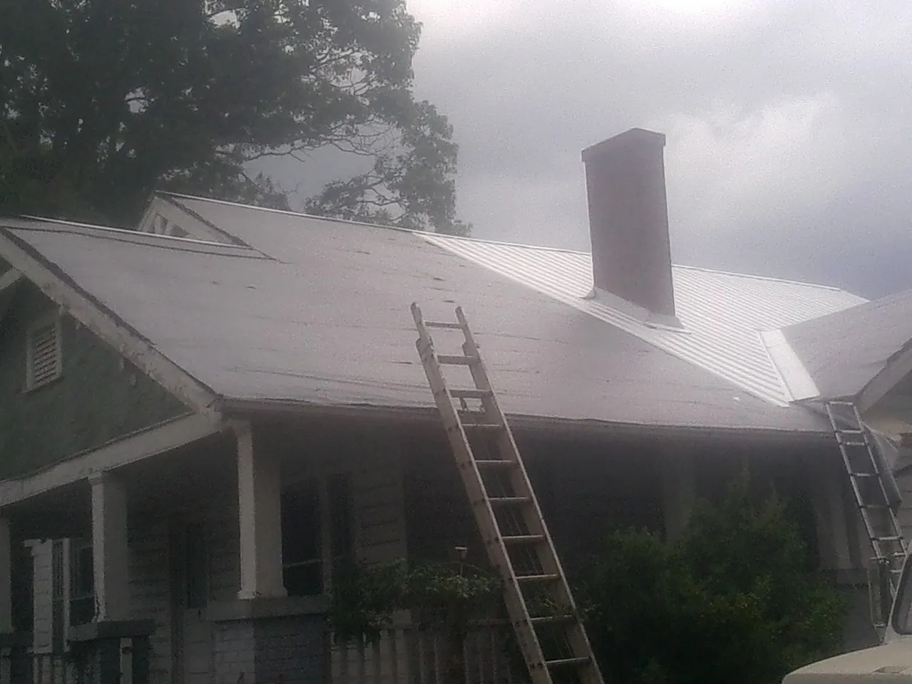 Ladders against a metal roof on an older home with a brick chimney in Woodland Park