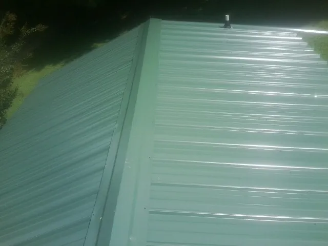 New green metal panels meeting at the ridge of a roof — Flat Roof Repair work by our crew in Woodland Park