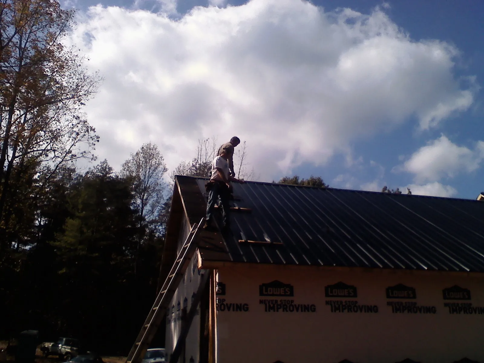 Roofer fastening dark metal panels high against a cloudy sky, from a Roof Inspection job in Woodland Park