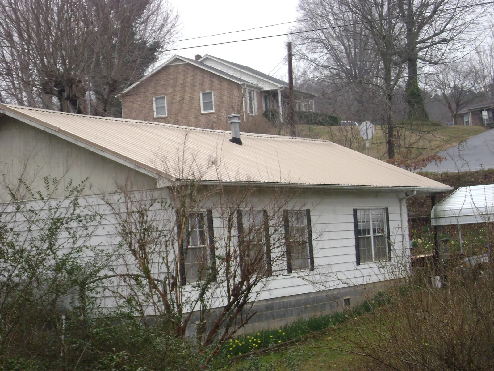Tan metal roof on a white sided house set into a hillside — Commercial Roofing by Roofing Brothers in Woodland Park