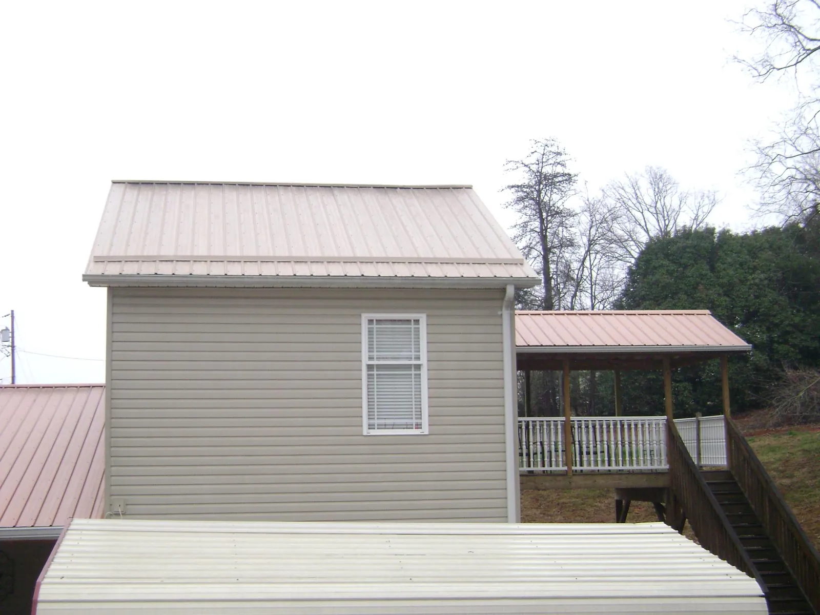 Tan metal roofs on a two story addition and attached porch, from a Roof Replacement job in Woodland Park